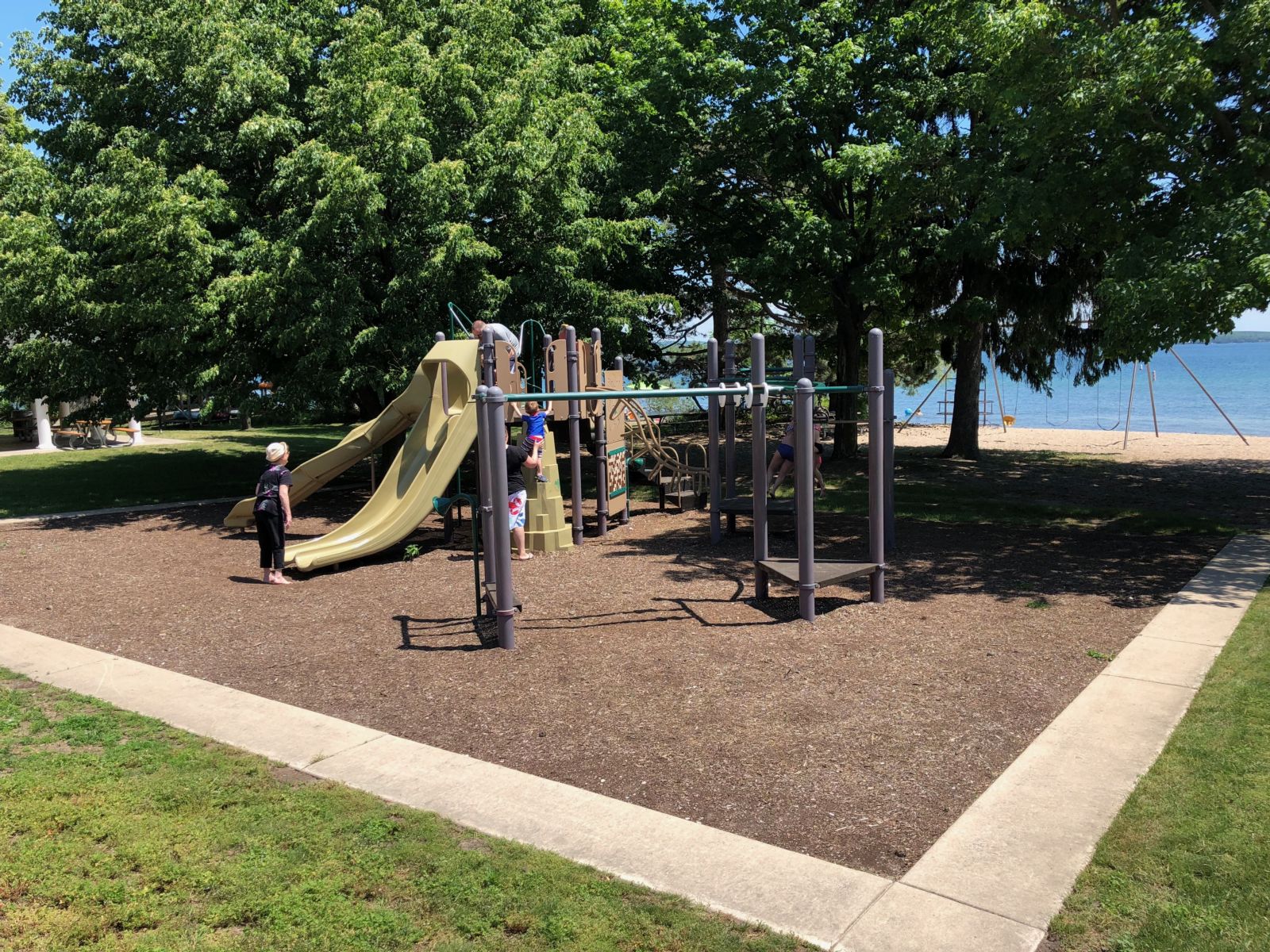 Depot Beach Playground surrounded by shady trees on the shore of Lake Charlevoix